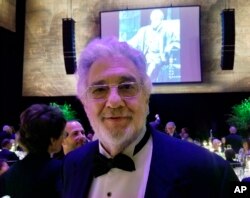 El tenor Placido Domingo posa para una foto delante de una imagen suya en la juventud cantando en la ópera "Otello" de Verdi. Abril 28 de 2019, en la Ópera Metropolitana de Nueva York.