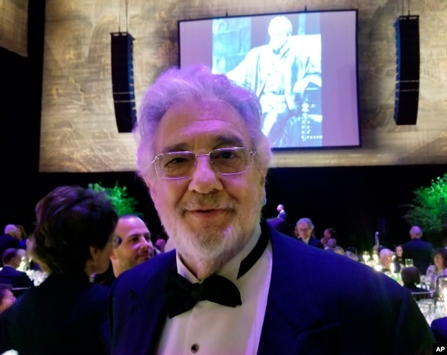 El tenor Placido Domingo posa para una foto delante de una imagen suya en la juventud cantando en la ópera "Otello" de Verdi. Abril 28 de 2019, en la Ópera Metropolitana de Nueva York.