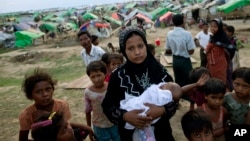 An internally displaced Rohingya woman holds her newborn baby surrounded by children in the foreground of makeshift tents at a camp for Rohingya people in Sittwe, northwestern Rakhine State, Burma, May13, 2013. 