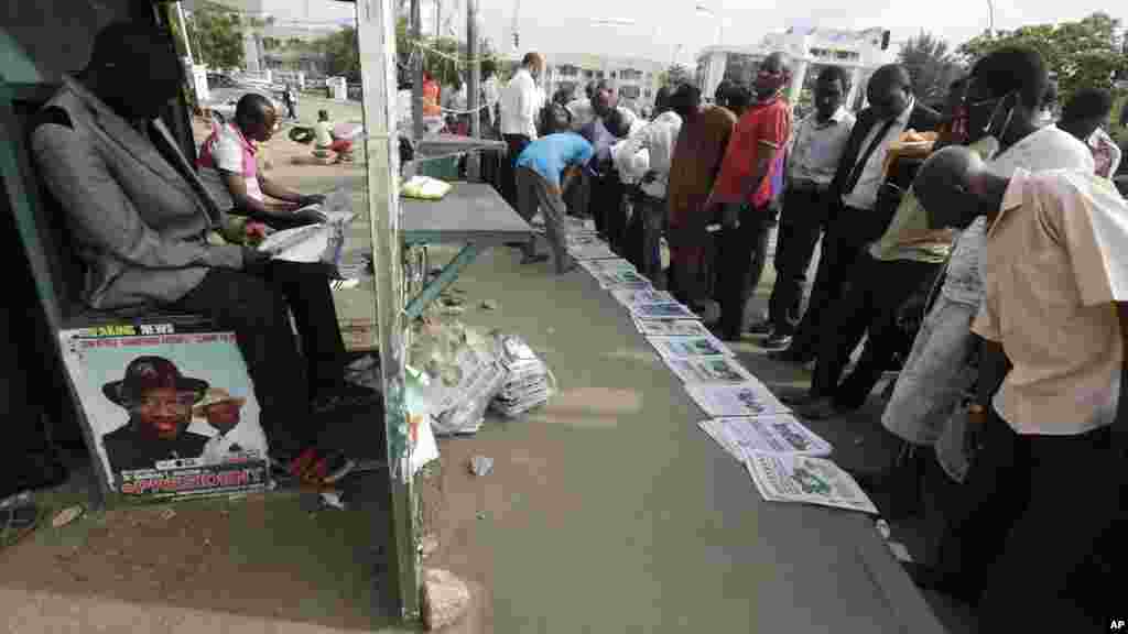 Pessoas lendo jornais com manchetes sobre as eleições nas ruas de Abuja.