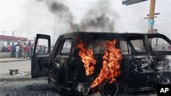 Local residents look on as a UN vehicle, set on fire by militant student supporters of Laurent Gbagbo, burns in the Riviera 2 neighborhood of Abidjan, 13 Jan 2011.