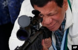 FILE - Philippine President Rodrigo Duterte checks the scope of a Chinese-made CS/LR4A sniper rifle during the presentation of thousands of rifles and ammunition by China to the Philippines, June 28, 2017, at Clark Air Base in northern Philippines.