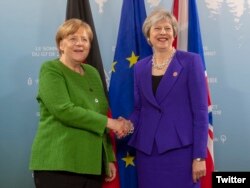 La canciller de Alemania, Angela Merkel (izq.) y la primera ministra de Gran Bretaña, Theresa May saludan antes de la reunión del G7 en Canadá. Junio 8 de 2018. Foto: @10DowningStreet.