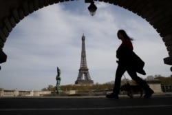 FILE - In this Tuesday, April 7, 2020 file photo, a woman walks her dog on a Paris bridge, with the Eiffel tower in background, during a nationwide confinement to counter the COVID-19.