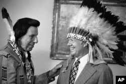 FILE - This photo shows Iron Eyes Cody, an Italian American famous for fabricating Native American identity,. Seen here presenting former President Jimmy Carter with a Native American headdress in the Oval Office in Washington on April 21, 1978.