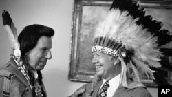 FILE - This photo shows Iron Eyes Cody, an Italian American famous for fabricating Native American identity. Seen here presenting former President Jimmy Carter with a Native American headdress in the Oval Office in Washington on April 21, 1978.