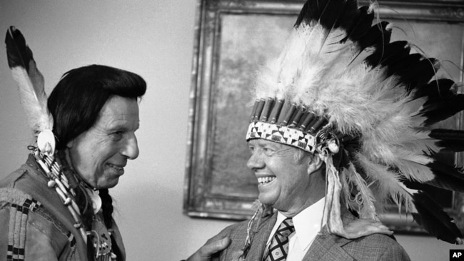FILE - This photo shows Iron Eyes Cody, an Italian American famous for fabricating Native American identity. Seen here presenting former President Jimmy Carter with a Native American headdress in the Oval Office in Washington on April 21, 1978.