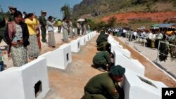 In this photo released by the Myanmar Defense Ministry, soldiers place urns containing ashes of soldiers fallen during a recent fighting against ethnic Kokang rebels at a military funeral in Lashio, Myanmar, Feb. 23, 2015.