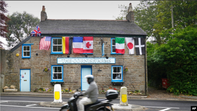 Një motoçiklist kalon përpara klubit të stolisur me flamujt e vendeve të G-7ës (Cornwall, Angli, 9 qershor 2021)