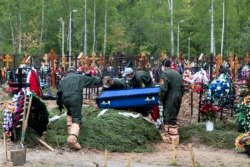 Grave diggers wearing protective suits carry a coffin of a COVID-19 victim for burial in the section of a cemetery reserved for coronavirus victims, outside Moscow, Russia, Tuesday, May 26, 2020.