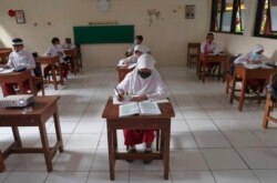 Siswa yang memakai masker duduk terpisah saat uji coba kelas dengan protokol COVID-19 di sebuah sekolah dasar di Jakarta, Jumat, 4 Juni 2021. (Foto: AP)