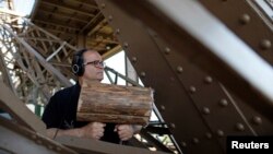 U.S. composer Joseph Bertolozzi makes sounds by striking the surface of the Eiffel Tower with a large log wrapped in lambswool for a musical project called 'Tower Music' in Paris, June 7, 2013.