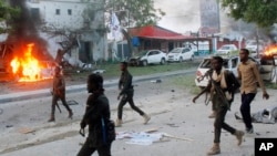 FILE - Security troops walk past burning cars after a fatal car bomb attack on a restaurant in Mogadishu, Somalia, May, 8, 2017. Al-Shabab militants claimed responsibility for the blast. Somalia's states on Sept. 8, 2018, suspended all ties with the central government, contending that it had taken its eye off the fight against al-Qaida-linked Islamist militants. 