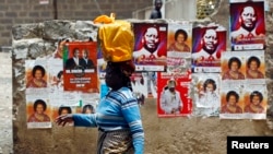 A woman walks past a wall covered with campaign posters on a street in Kenya's capital Nairobi March 3, 2013.