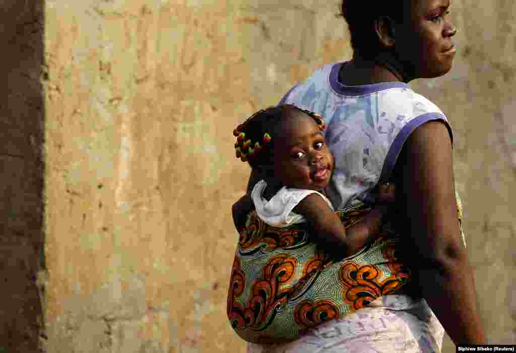 Uma mulher caminha com um bebé amarrado com pano em Luanda.