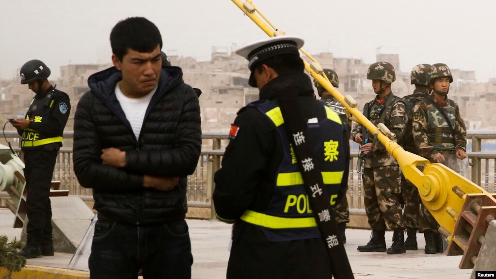 在中国新疆维吾尔自治区喀什的一条街上,警察检查一名男子的身份证,旁边有安全人员(2017年3月24日)