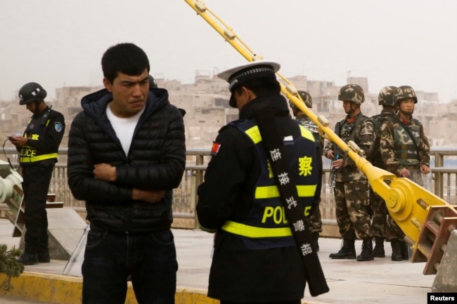 在中国新疆维吾尔自治区喀什的一条街上，警察检查一名男子的身份证，旁边有安全人员（2017年3月24日）