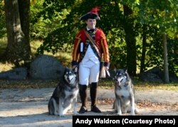 A citizen volunteer, dressed as an 18th century British soldier, poses for a picture with a couple of canine visitors at Minute Man National Historical Park in Concord, Massachusetts.