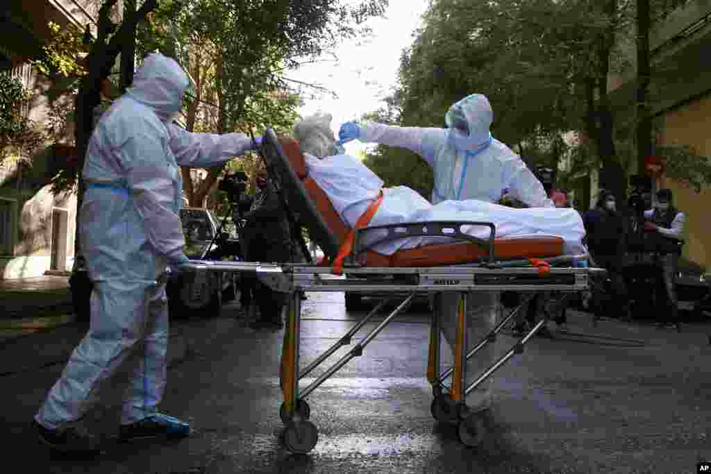 A paramedic with a special suit to protect against coronavirus, adjusts the face mask of a patient as his colleague pulls the stretcher out of a nursing home where dozens of elderly people have been found positive to COVID-19, in Athens, Greece.