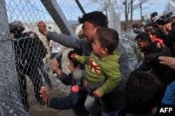 A man from Afghanistan carrying a baby cries as he pushes against the fence at the Greece-Macedonia border during a demonstration near the village of Idomeni, northern Greece, on February 22, 2016.