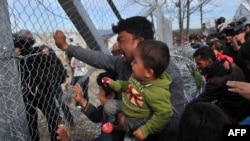 FILE - A man from Afghanistan carrying a baby cries as he pushes against the fence at the Greece-Macedonia border during a demonstration near the village of Idomeni, northern Greece, Feb. 22, 2016.