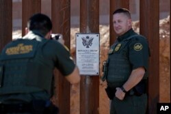 FILE - Border Patrol agent Michael Sullivan (R) poses for a picture next to a plaque adorning a newly fortified border wall structure in Calexico, Calif., Oct. 26, 2018.