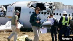 FILE - US National Transportation Safety Board (NTSB) investigators stand at the scene of the Asiana Airlines Flight 214 crash site at San Francisco International Airport in San Francisco, July 7, 2013.