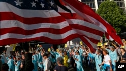 Para pengunjuk rasa mengenakan kostum ala Patung Liberty berbaris di bawah bendera AS, saat melakukan aksi demo di pusat kota Brussel, Rabu, 24 Mei 2017, menjelang kunjungan Presiden AS Donald Trump dan KTT NATO yang akan berlangsung pada hari Kamis, 25 Mei 2017, hari ini. (AP Photo / Peter Dejong)