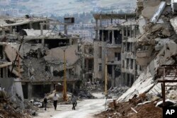 FILE - Residents walk through rubble with damaged electricity lines at the mountain resort town of Zabadani in the Damascus countryside, Syria, May 18, 2017.