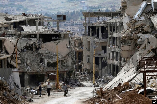 FILE - Residents walk through rubble with damaged electricity lines at the mountain resort town of Zabadani in the Damascus countryside, Syria, May 18, 2017.