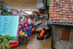 Seorang pria mencoba menangkap ternak angsa miliknya dari atap rumah setelah hujan mengakibatkan banjir di Jakarta, 1 January 2020. (Foto: AFP)