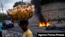 A street vendor walks past a barricade of burning tires during a demonstration against high prices and fuel shortages in Port-au-Prince, on Oct. 21, 2021. 