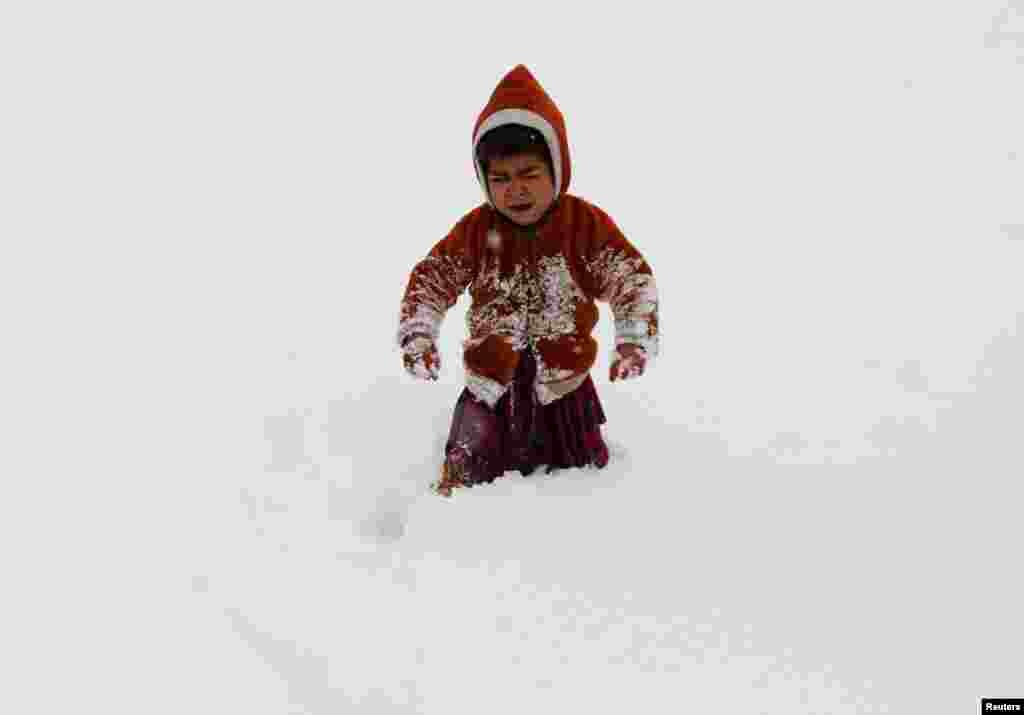 An internally displaced Afghan child cries as he gets stuck in waist-deep snow outside his shelter during a snowfall in Kabul.