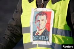 A "Yellow Vest" protester sports an image of French President Emmanuel Macron, with "Diktatur," the German word for "Dictatorship," written on it, in Paris, France, Nov. 17, 2018.