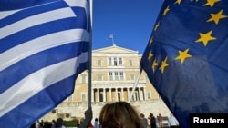 A woman waves a Greek national flag and a European Union flag during a rally outside the Parliament, calling on the government to clinch a deal with its international creditors and secure Greece's future in the Eurozone, in Athens, Greece, June 18, 2015.