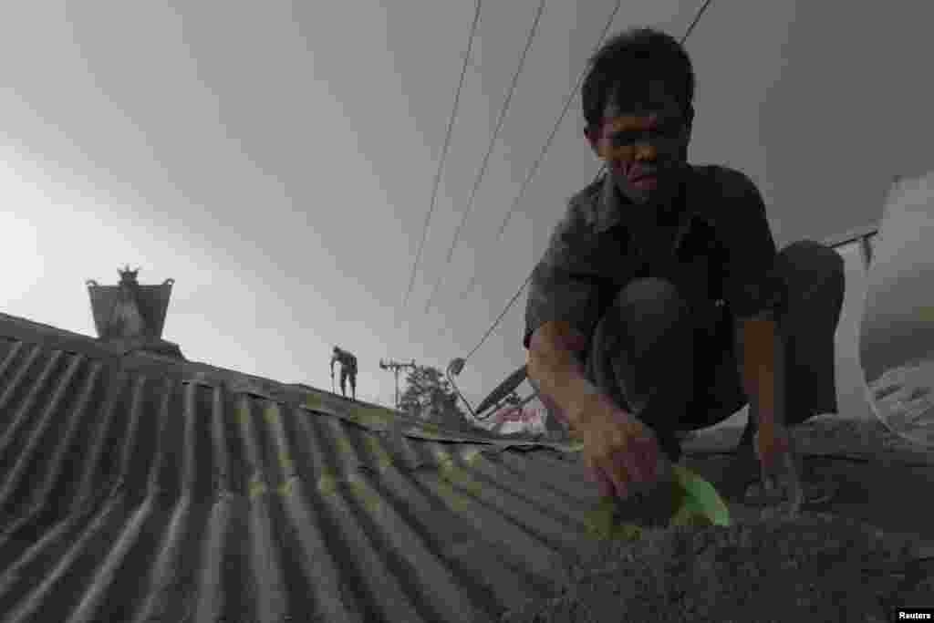 Villagers clean a roof of ash from a Mount Sinabung eruption as seen at Sibintun village in Karo district, Indonesia, Jan. 14, 2014. 