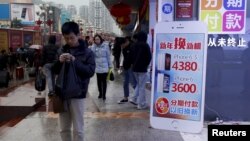 A man checks his smartphone outside a store promoting the Apple iPhone products in the southern Chinese city of Shenzhen, Jan. 26, 2016. 