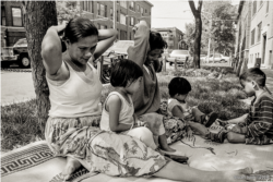 Cambodian women and children relax and play between the street and sidewalk outside their apartment building in the 1990s on Argyle Street in the Uptown neighborhood of Chicago.