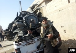 An armed jihadist stands next to the wreckage of a Syrian government forces aircraft which was shot down by militants of the Islamic State (IS) group over the Syrian town of Raqa on September 16, 2014. The plane crashed into a house in the Euphrates Valle