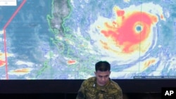 A member of the Philippine Air Force stands in front of a satellite image of Typhoon Mangkhut, locally named Typhoon Ompong, at the National Disaster Risk Reduction and Management Council operations center in metropolitan Manila, Philippines on Thursday, Sept. 13, 2018. (AP Photo/Aaron Favila)