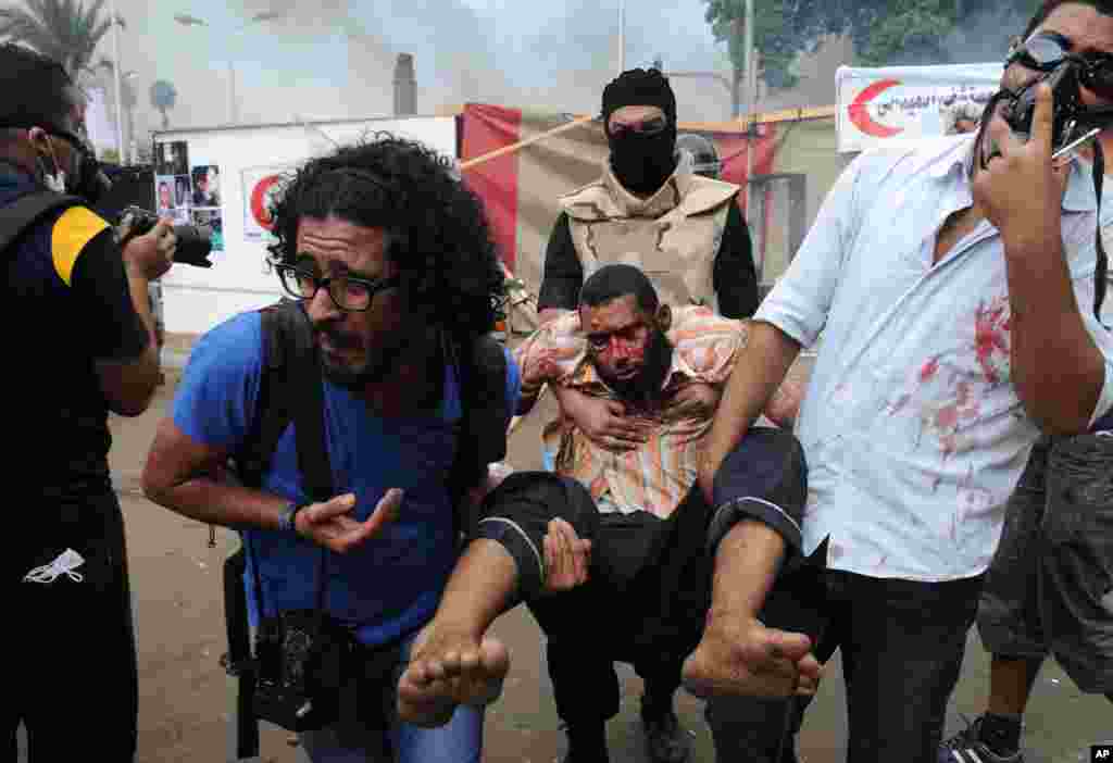 Supporters of ousted Islamist President Mohammed Morsi carry another as Egyptian security forces clear a sit-in camp set up near Cairo University in Cairo's Giza district, Egypt, Wednesday, Aug. 14, 2013. Egyptian police in riot gear swept in with armored