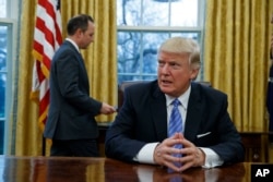 President Donald Trump sits at his desk as he waits for White House Chief of Staff Reince Priebus, left, to deliver three executive orders for his signature, Jan. 23, 2017, in the Oval Office of the White House in Washington.