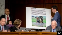 Senator Chris Coons (kiri) berbicara sementara seorang asistennya menayangkan sebuah poster yang menampilkan contoh iklan Facebook yang menyesatkan dalam sidang dengar pendapat Komite Hukum di Capitol Hill, Washington DC, 31 Oktober 2017.