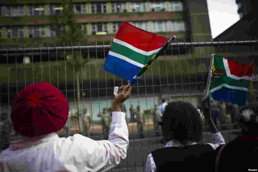 Women wave South African national flags before the cortege carrying the coffin of former South African President Nelson Mandela passes by in Pretoria, Dec. 11, 2013.