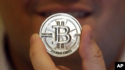  FILE - A man holds a token bearing the symbol of a cryptocurrency at his shop in Sandy, Utah. 
