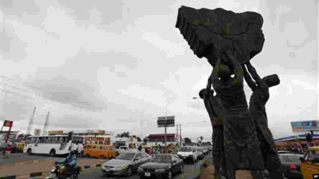 Traffic passes a statue depicting Nigeria's three major tribes, the Hausa, the Igbo and the Yoruba, lifting up a map depicting Nigeria.
