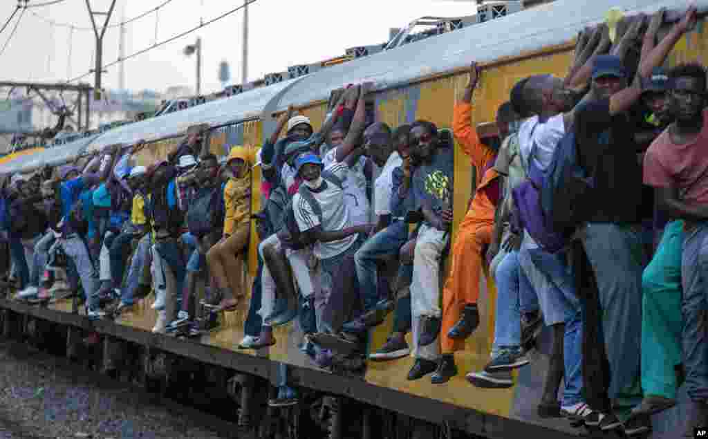 Train commuters hold on to the side of an overcrowded passenger train in Soweto, South Africa.