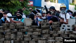 Manifestantes se protegen detrás de una barricada durante una protesta antigubernamental en Managua, Nicaragua.