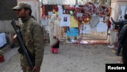 A soldier stands near a woman reading messages left by people for the victims of the Taliban attack on a school, in Peshawar, Pakistan, Dec. 23, 2014. 