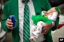 Joey Homans holds his 3-month-old granddaughter Caroline Homans in one hand and a beer in the other before the start of the Savannah St. Patrick's Day parade, March 16, 2019, in Savannah, Ga.